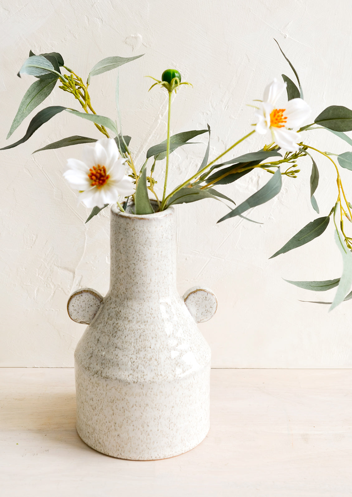 A speckled ceramic vase with flowers.
