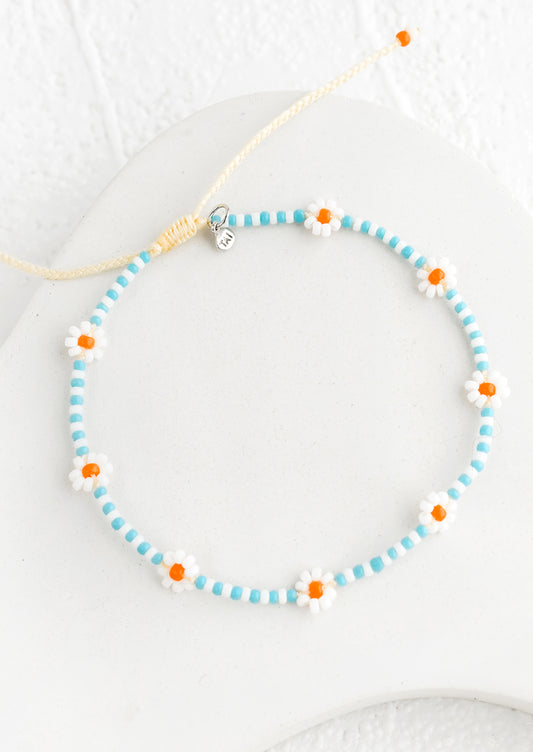 A beaded bracelet in blue and white with orange flowers.