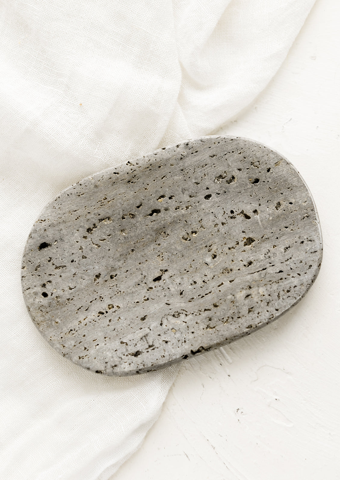 An oval-shaped soap dish in grey travertine.