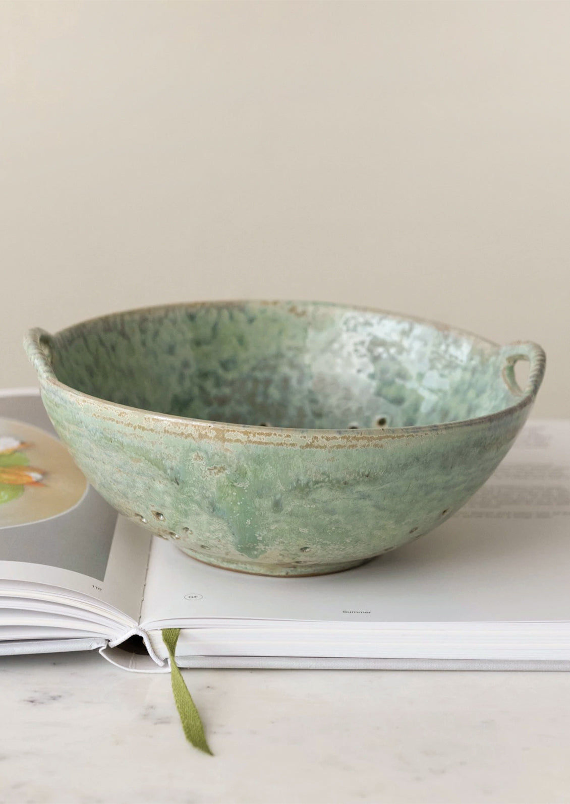 A large ceramic colander in mottled aqua glaze.