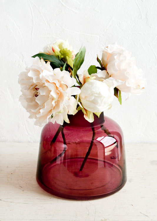 A berry colored glass vase with peonies.