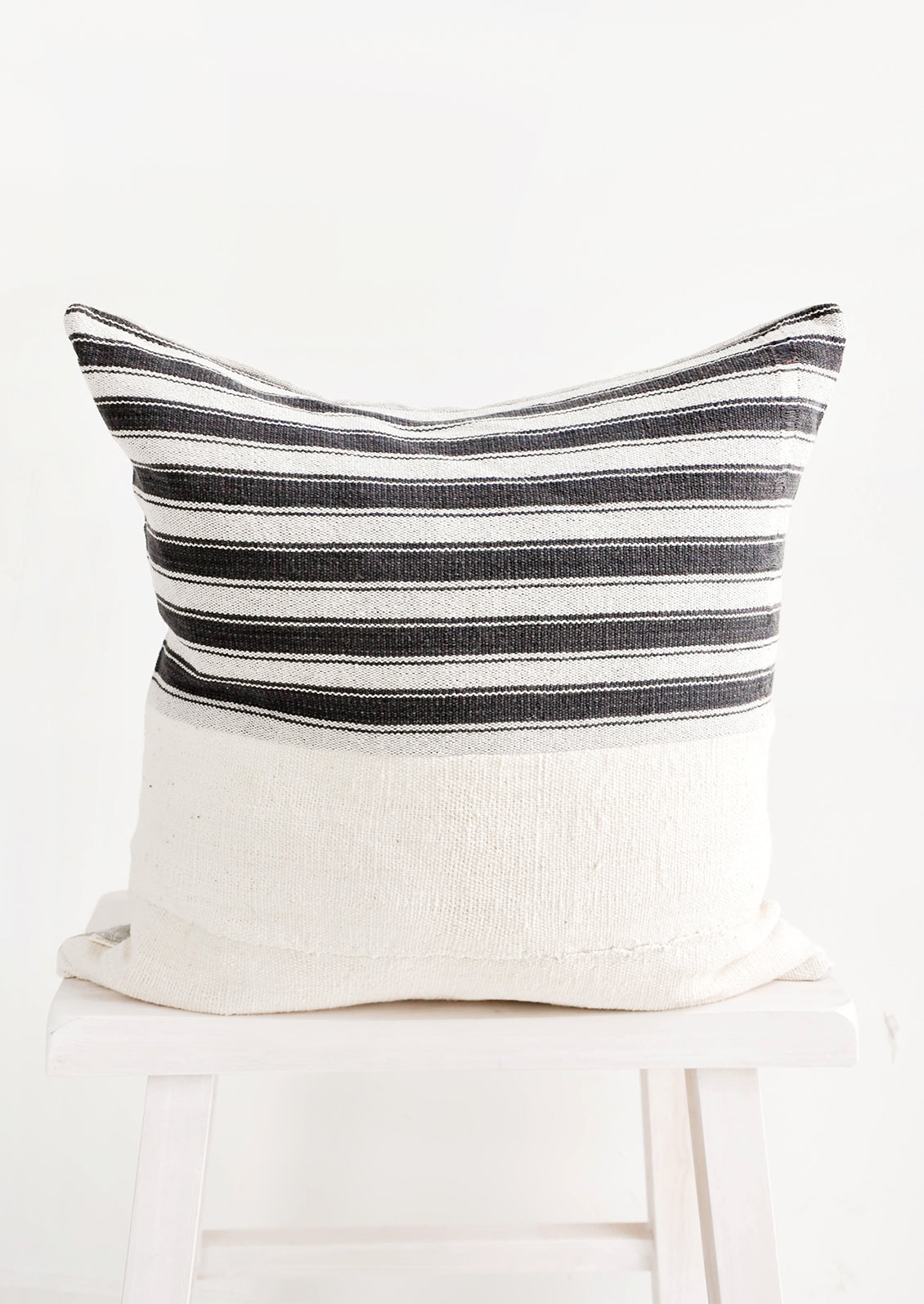 Square throw pillow with white and black striped top half and plain mudcloth bottom half