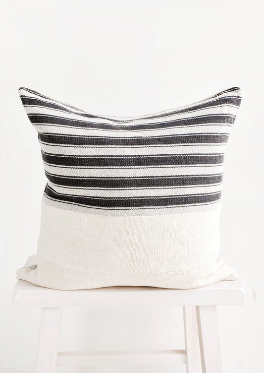 Square throw pillow with white and black striped top half and plain mudcloth bottom half