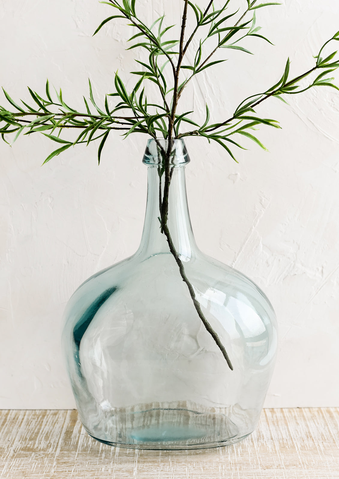 A large bottle shaped glass vase with branch.
