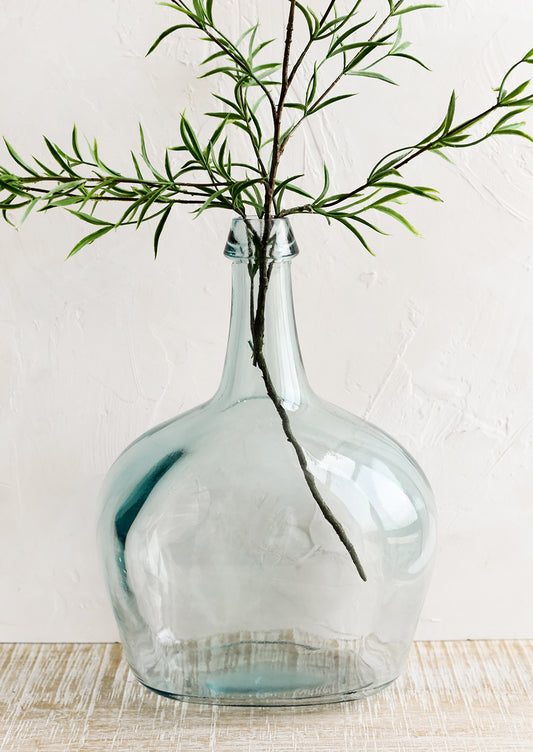 A large bottle shaped glass vase with branch.