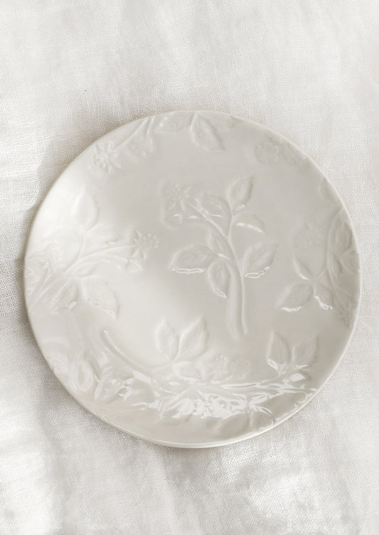 A round ceramic dessert plate in ivory with tonal raspberry pattern.