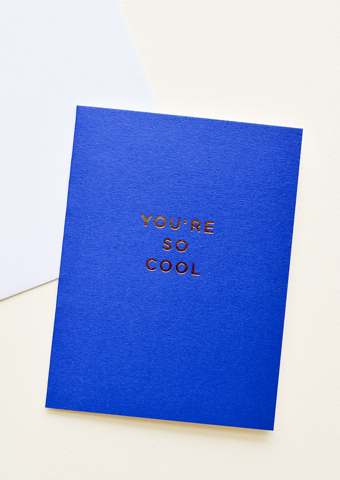 Notecard with gold foil text "You're so cool" on bright cobalt background, with white envelope.